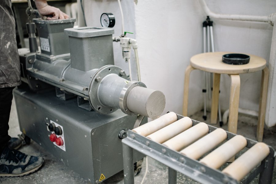 A pug mill extruding a dense column of clay onto a roller conveyor