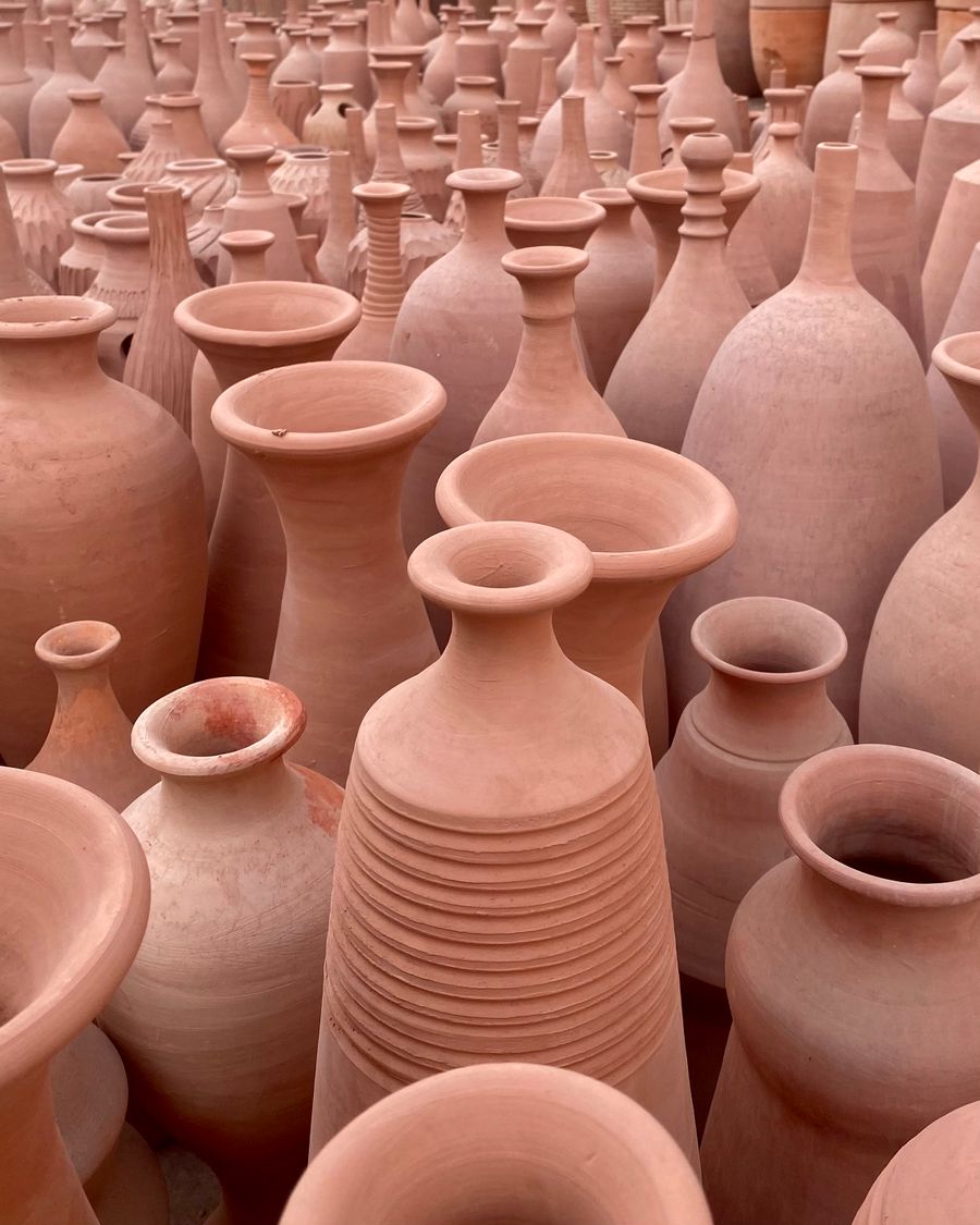 Rows of unglazed, warm reddish-brown terracotta vases and bottles, unfired body color visible
