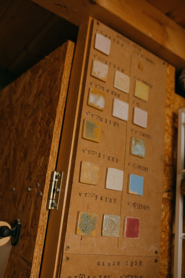 A wooden board with rows of small labeled glaze test tiles showing a range of colors and surface effects