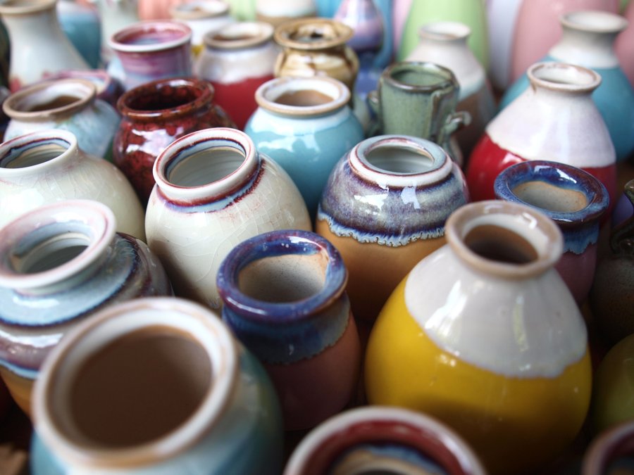 A dense overhead view of many small glazed ceramic vessels in a wide range of colors and glaze effects
