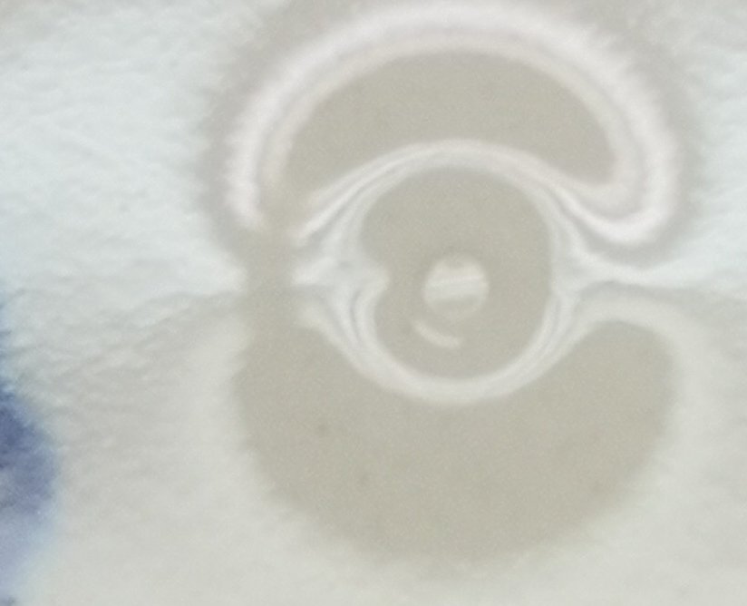 Close-up of an unbroken glassy blister dome on a glazed surface, with a smaller pit beside it