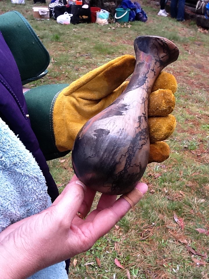 A small pot with mottled black smoke-clouding and pinkish-tan fire marks, held fresh out of a pit firing
