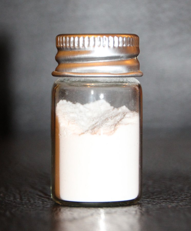 A small glass jar containing fine white silicon dioxide powder