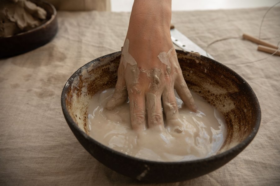 A hand dipped into a bowl of smooth, liquid clay slip