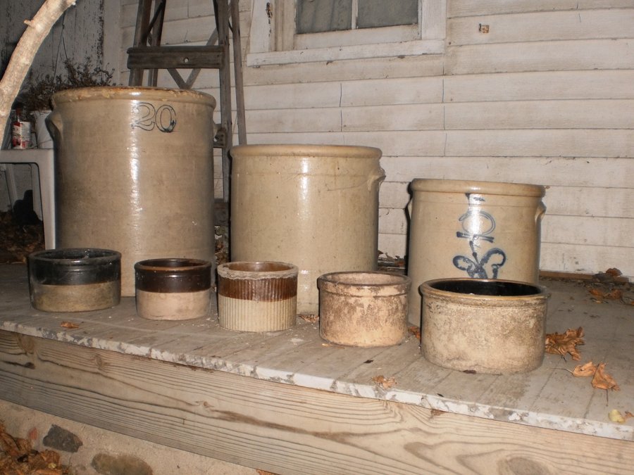 A row of antique salt-glazed stoneware crocks in grey, tan, and buff tones