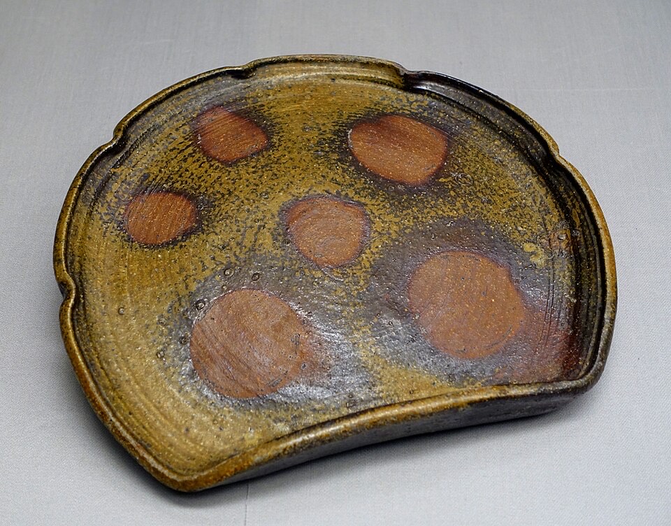 An unglazed stoneware dish with natural olive-toned ash glaze and circular reddish fire-marks left by wadding during a wood firing